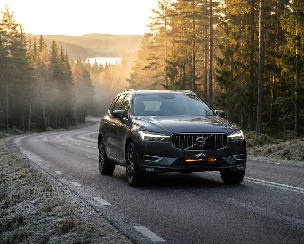 LUXTAR TICON license plate light bar on a dark grey Volvo SUV driving on a winding road at sunset.