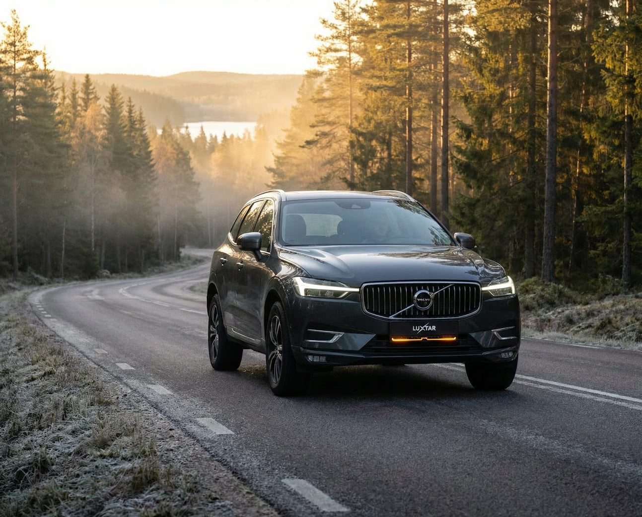 LUXTAR TICON license plate light bar on a dark grey Volvo SUV driving on a winding road at sunset.